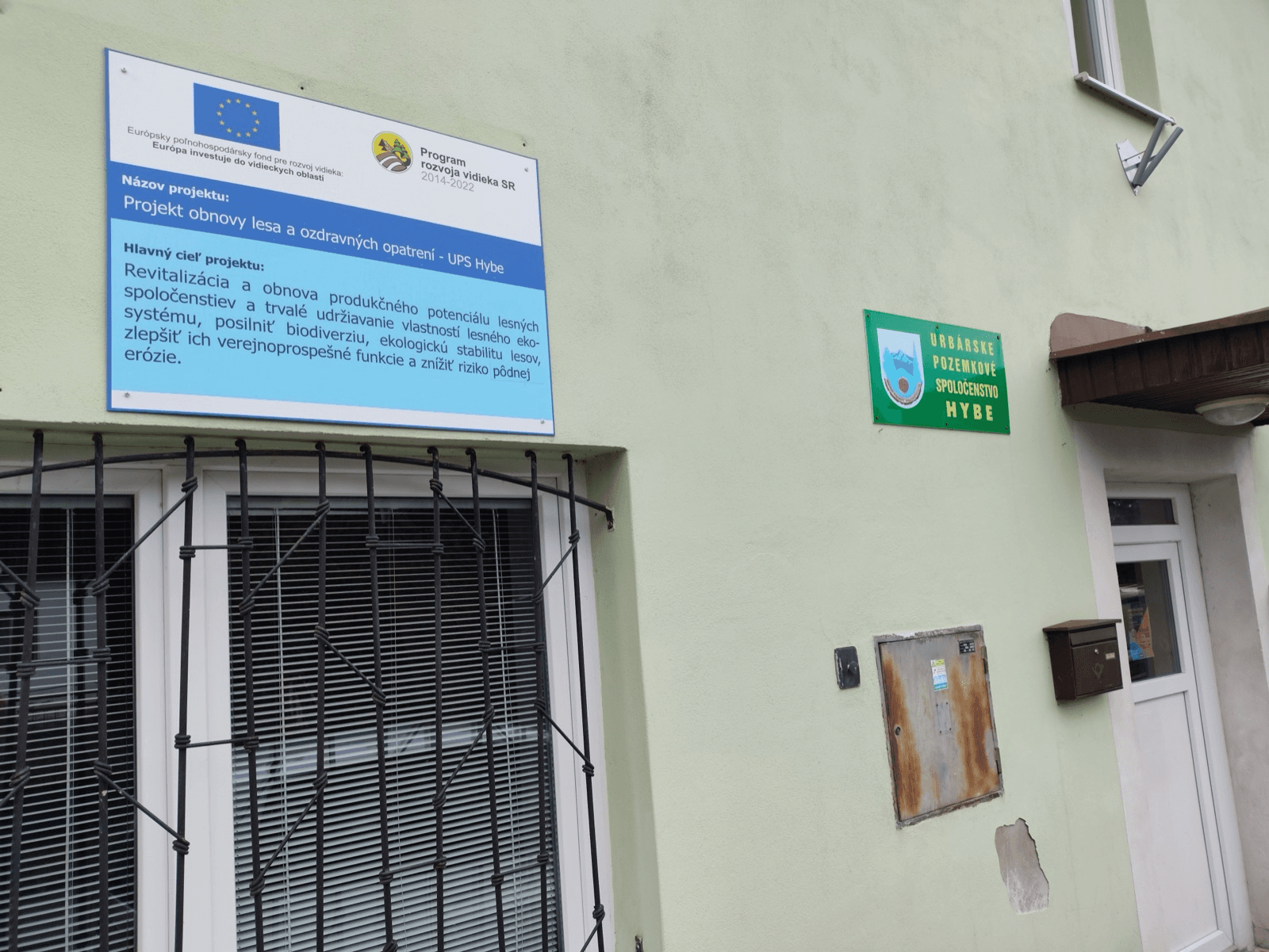 Informačná tabuľa projektu „Projekt obnovy lesa a ozdravných opatrení – UPS Hybe" na budove spoločenstva